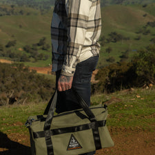 Person holding a green duffel bag with a mountainous landscape in the background