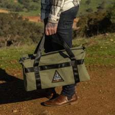 Person holding a green and black bag outdoors with a scenic background