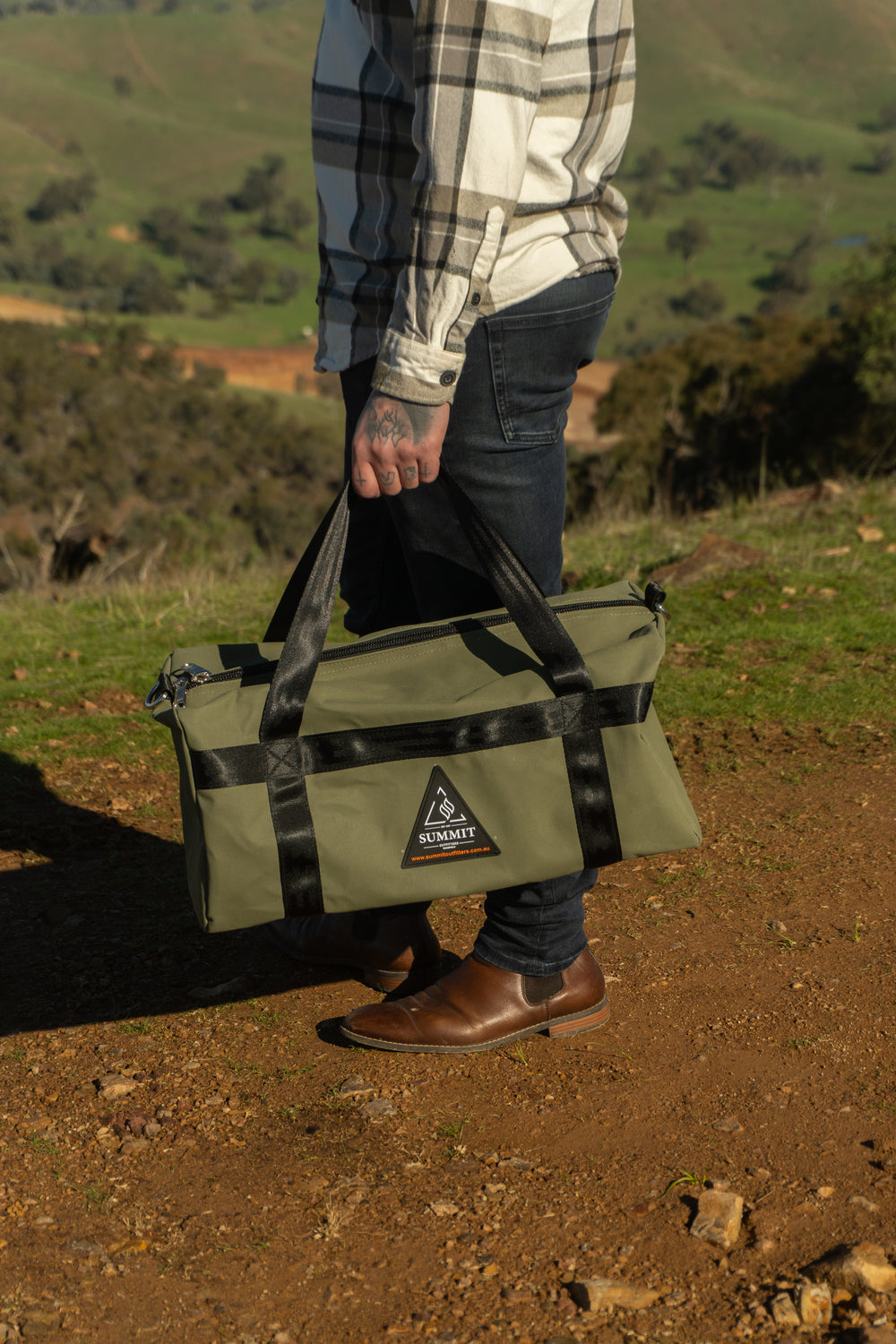 Person holding a green and black bag outdoors with a scenic background
