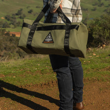 Person holding a green duffel bag with a scenic background