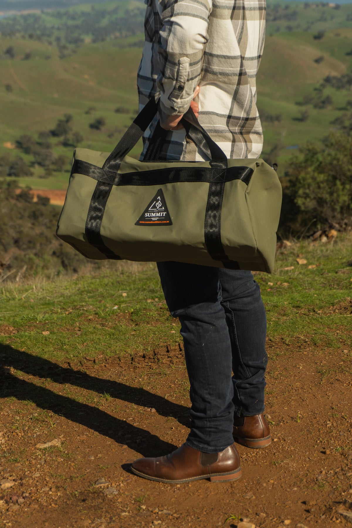 Person holding a green duffel bag with a scenic background