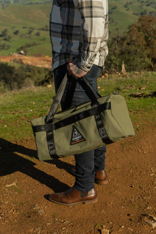 Person holding a green bag with a logo in a natural setting