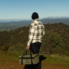 Person holding a green bag with a mountainous landscape in the background