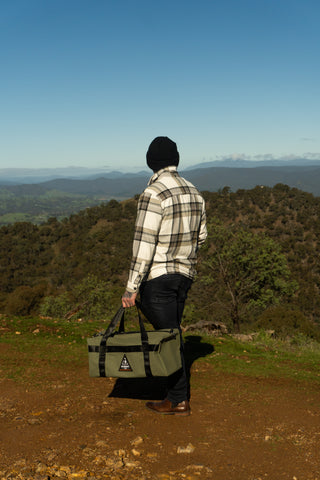 Person holding a green bag with a mountainous landscape in the background