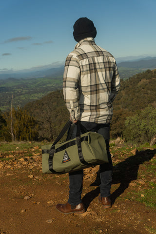 Person standing on a hill with a scenic view, holding a green duffel bag.