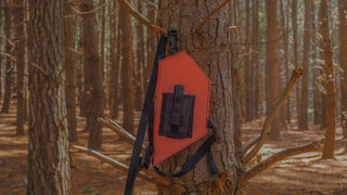 Orange hunting radio holster attached to a tree in a forest