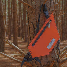 Orange radio holster hanging on a tree branch in a forest setting