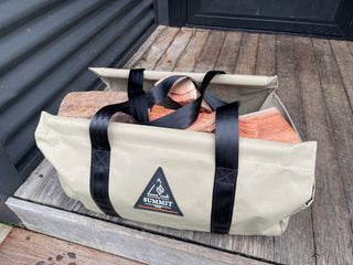 Beige carrying bag with black straps holding firewood, branded 'Summit', on a wooden step.