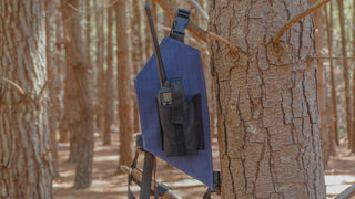Blue radio holster attached to a tree in a forest setting