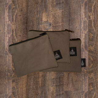 Three brown canvas pencil cases with a zipper closure, placed on a wooden surface.