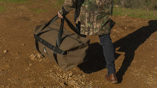 Person in camouflage holding a large brown bag outdoors on a dirt path