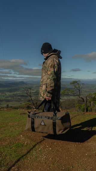 Person in camouflage jacket holding a bag with a scenic landscape in the background