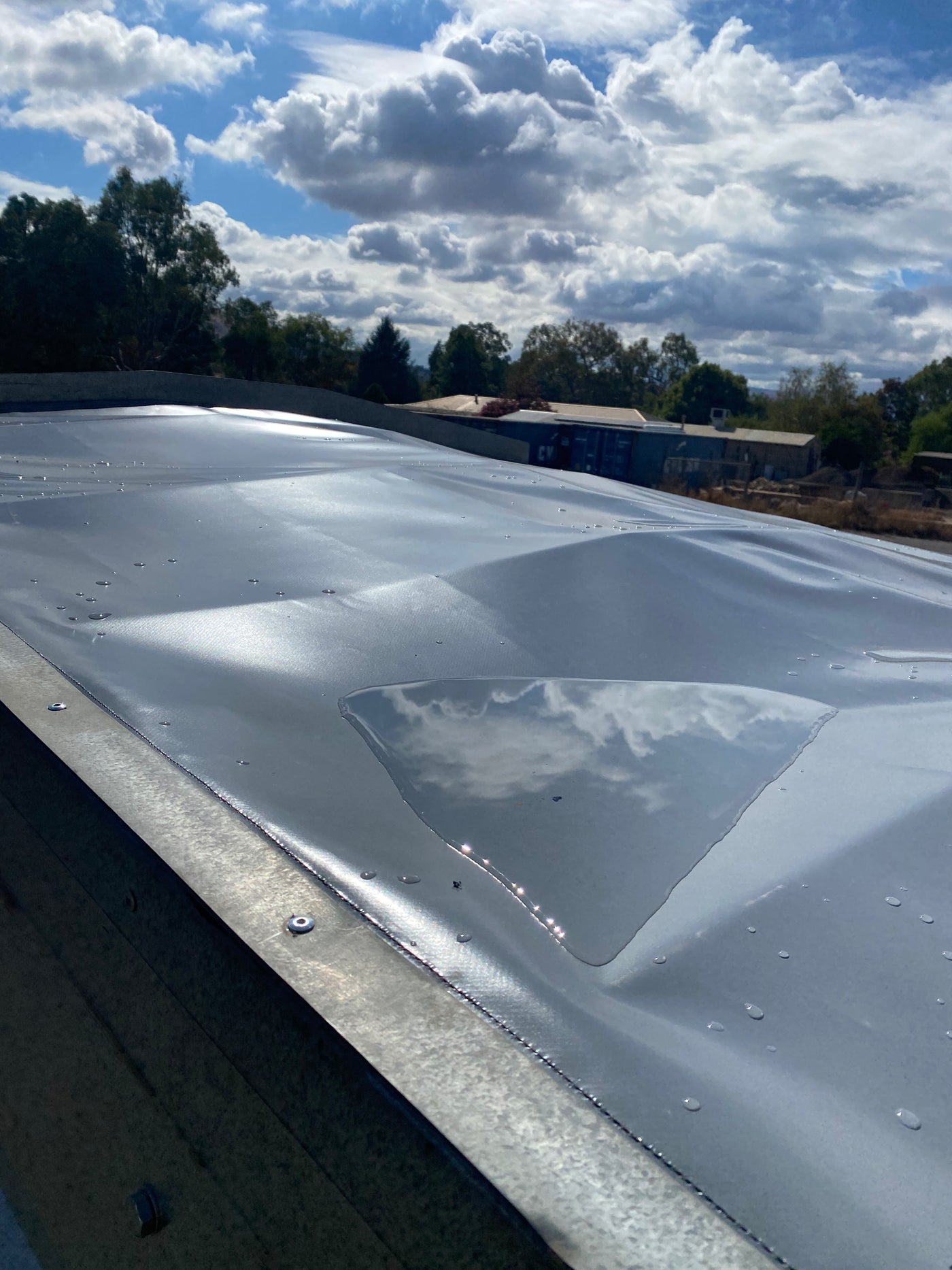 Canvas truck cover sheet with water puddle reflecting cloudy sky outdoors