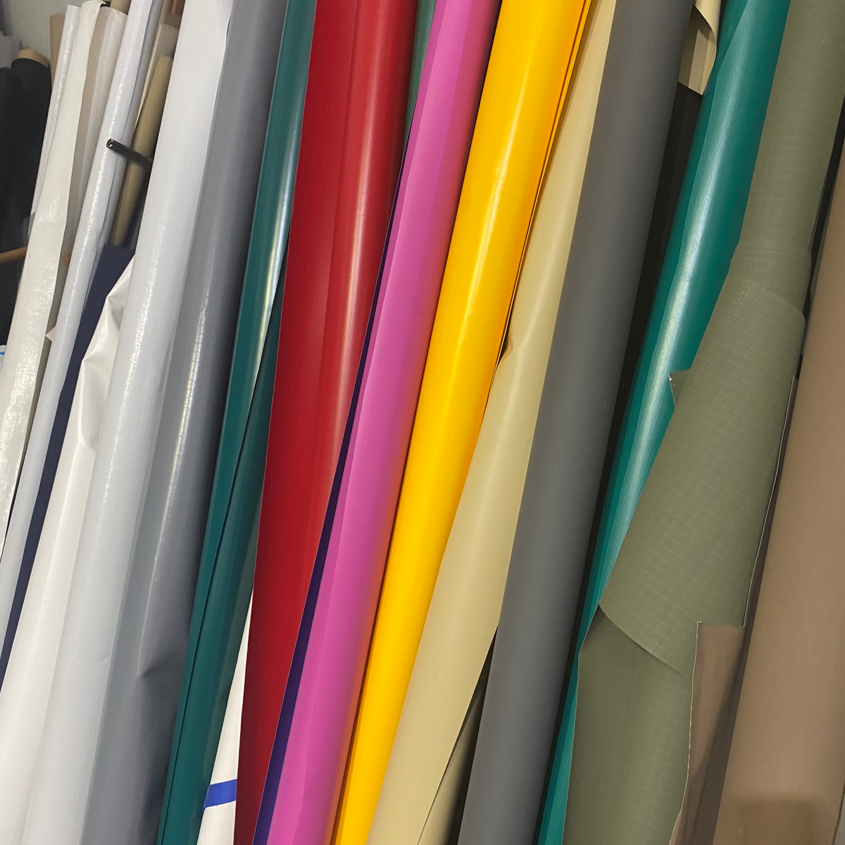 Glossy PVC canvas rolls in assorted colors stacked vertically in workshop