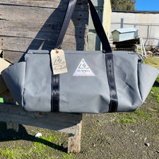 grey coloured canvas firewood carrier bag with black strapped handles and small triangle summit outfitters pvc logo patch on front of product, hanging off wooden palette