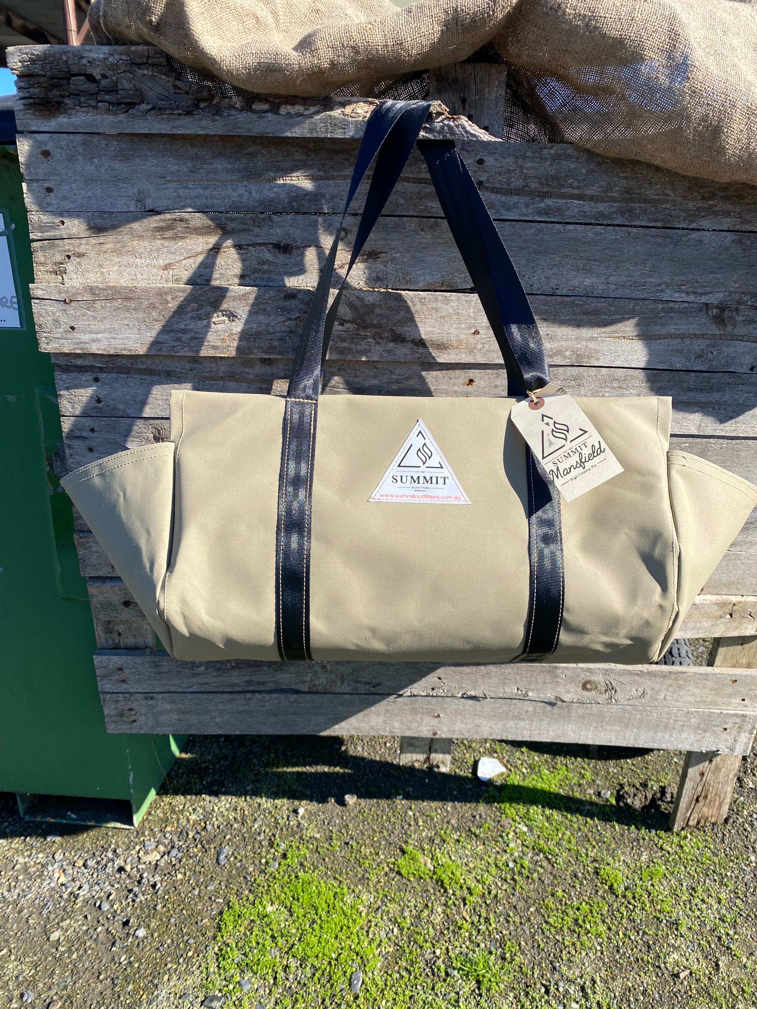 beige coloured canvas firewood carrier bag with black strapped handles and small triangle summit outfitters pvc logo patch on front of product, hanging off wooden palette