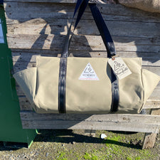 beige coloured canvas firewood carrier bag with black strapped handles and small triangle summit outfitters pvc logo patch on front of product, hanging off wooden palette