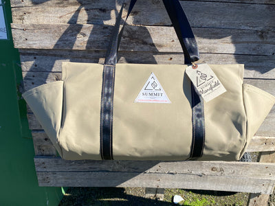beige coloured canvas firewood carrier bag with black strapped handles and small triangle summit outfitters pvc logo patch on front of product, hanging off wooden palette