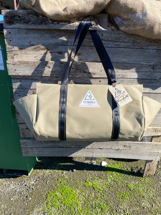 beige coloured canvas firewood carrier bag with black strapped handles and small triangle summit outfitters pvc logo patch on front of product, hanging off wooden palette