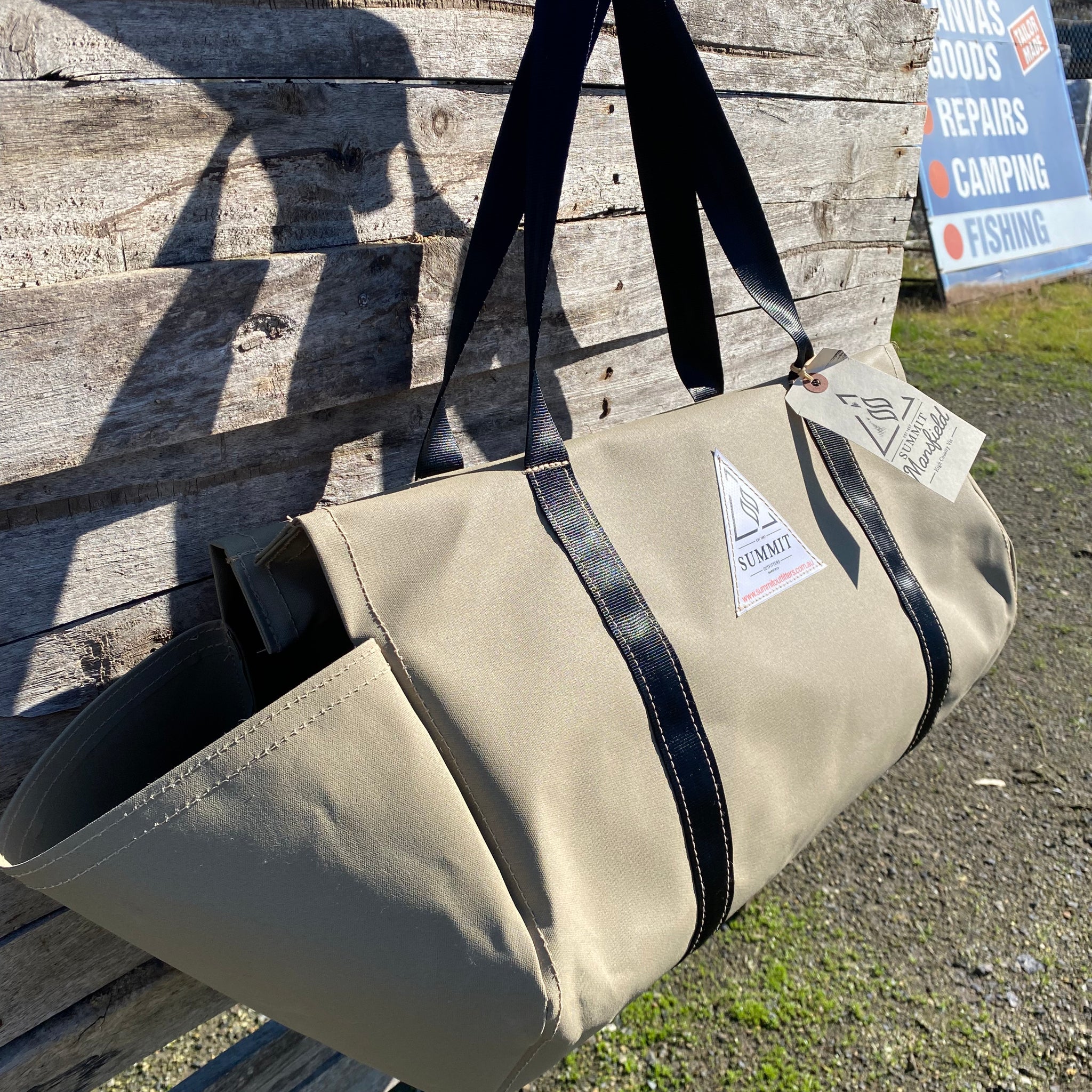 beige coloured canvas firewood carrier bag with black strapped handles and small triangle summit outfitters pvc logo patch on front of product, hanging off wooden palette