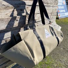 beige coloured canvas firewood carrier bag with black strapped handles and small triangle summit outfitters pvc logo patch on front of product, hanging off wooden palette