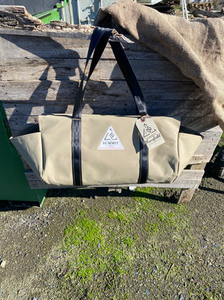 beige coloured canvas firewood carrier bag with black strapped handles and small triangle summit outfitters pvc logo patch on front of product, hanging off wooden palette