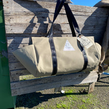 beige coloured canvas firewood carrier bag with black strapped handles and small triangle summit outfitters pvc logo patch on front of product, hanging off wooden palette