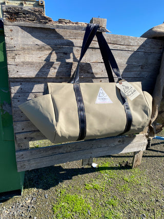 beige coloured canvas firewood carrier bag with black strapped handles and small triangle summit outfitters pvc logo patch on front of product, hanging off wooden palette