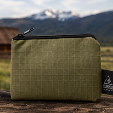 Green pencil case with black zipper on a wooden surface with a mountainous background