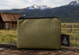 Green pencil case with black zipper on a wooden surface with a mountainous background