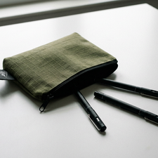 Green pencil case with three black pens on a white surface