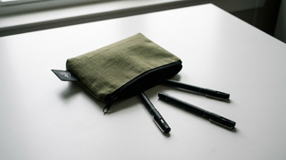 Green pencil case with three black pens on a white surface