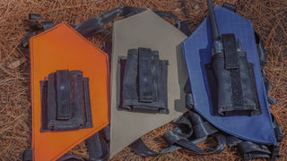 Three radio holsters in orange, sand, and blue with radio holders on a pine needle covered floor