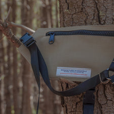Beige radio holster with black straps attached to a tree in a forest setting