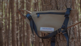 Beige radio holster with black straps attached to a tree in a forest setting