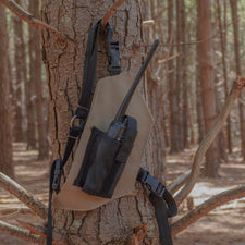Beige radio holster attached to a tree in a forest setting