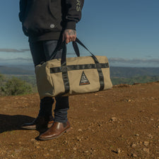 Person holding a beige bag with a logo in a scenic outdoor setting