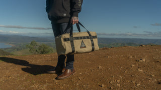Person holding a beige bag with a logo in a scenic outdoor setting